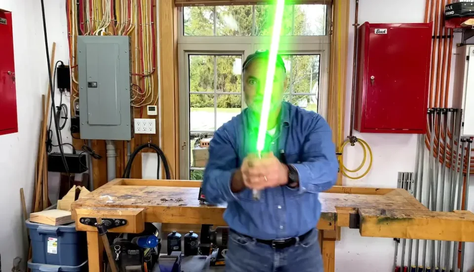 Person holding green light saber in workshop.