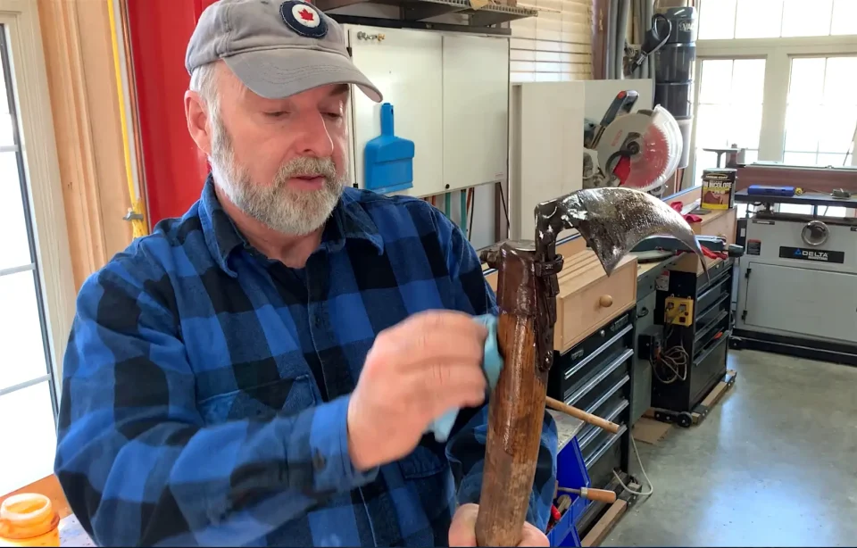 Man polishing rustic curved tool in workshop.