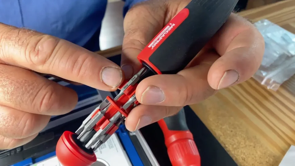 Hands holding multi-bit screwdriver with red handle.