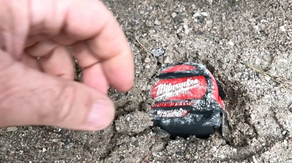 Retrieving buried Milwaukee tape measure from dirt.