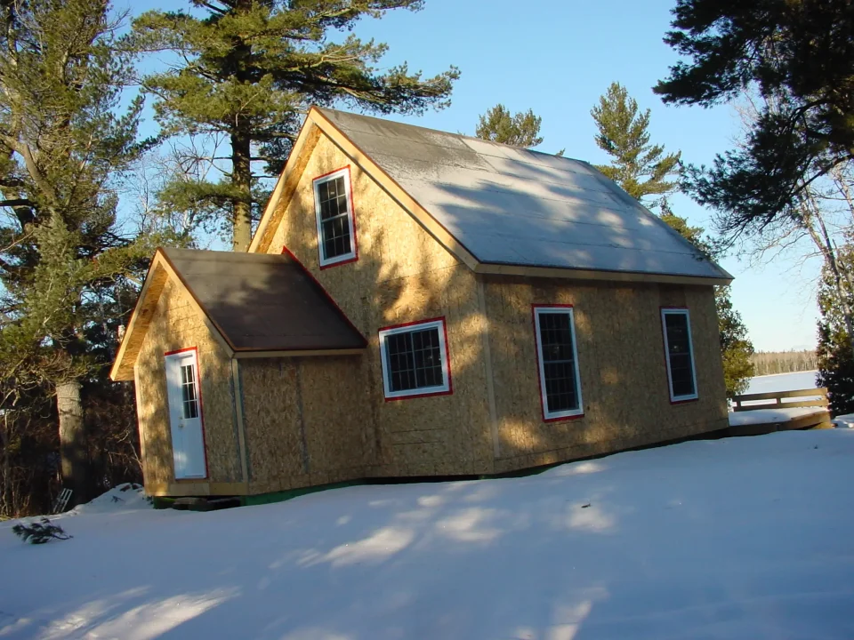 Snow-covered cabin in forested area during winter.