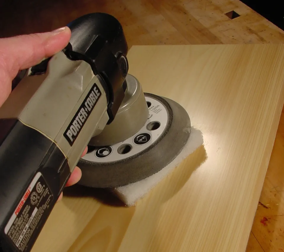 Hand holding power sander on wooden surface.