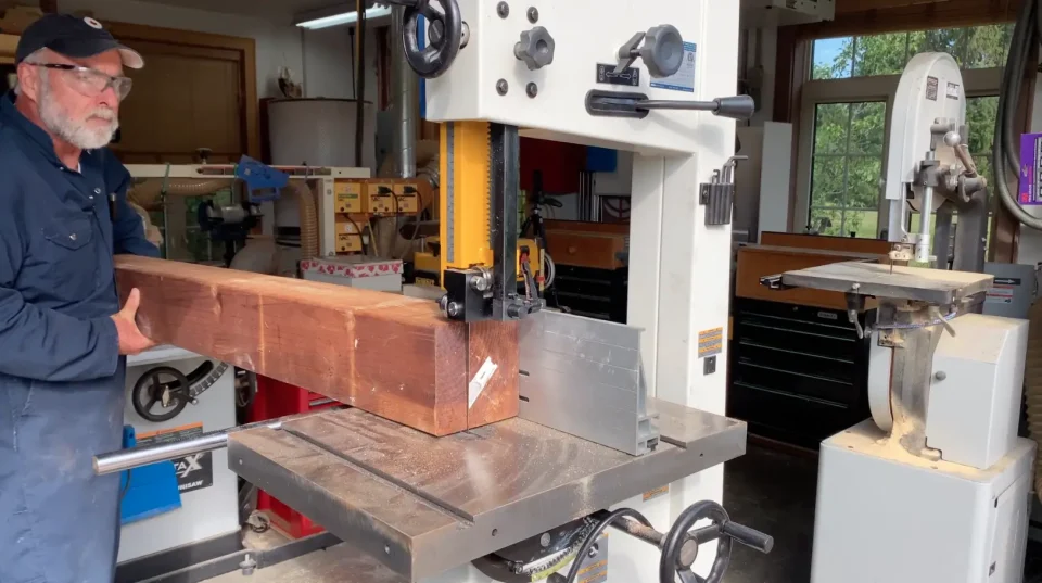 Man using bandsaw to cut wooden beam.