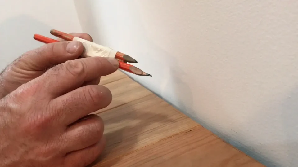 Dual pencils outlining a line on white wall.