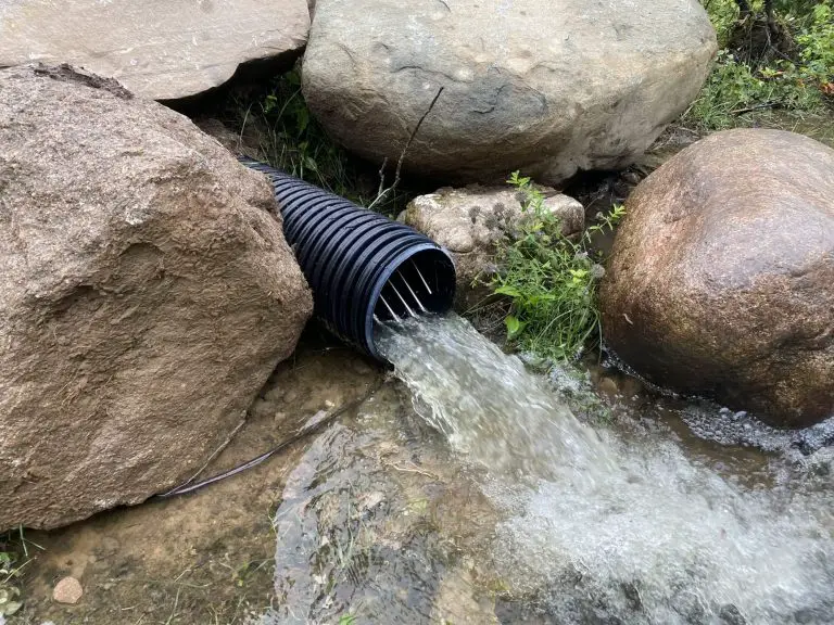 Water flows from drainage pipe between rocks.