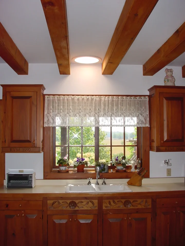 Cozy kitchen with wooden beams and window view.