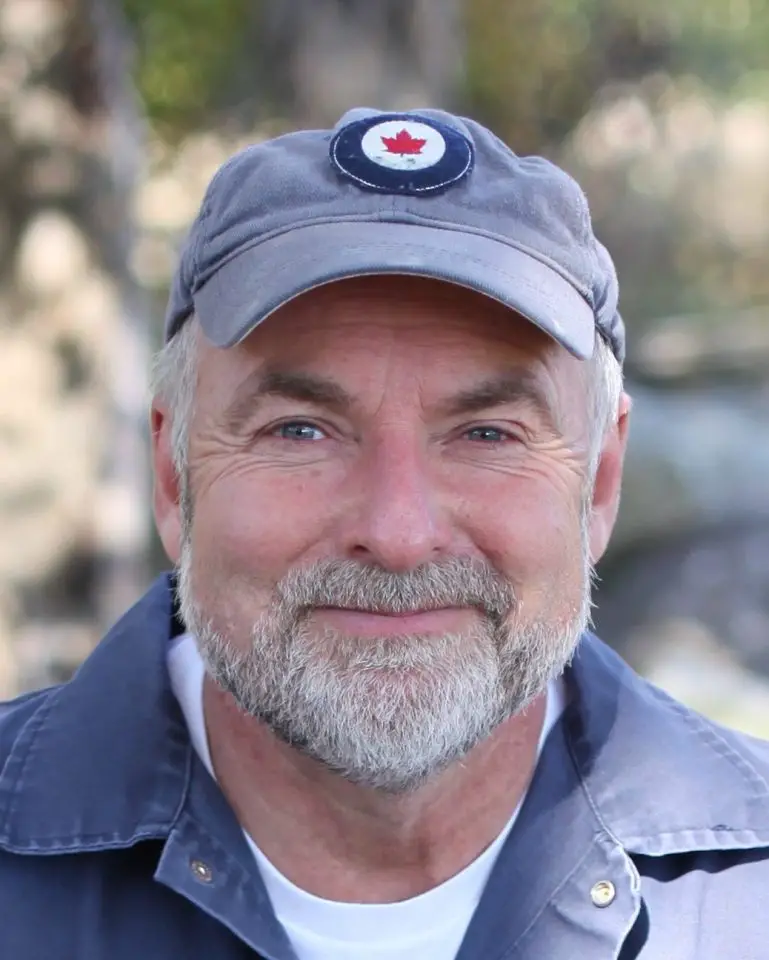 Smiling man wearing cap with maple leaf emblem.