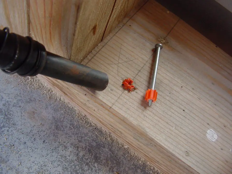 Nail with orange clip on wooden surface