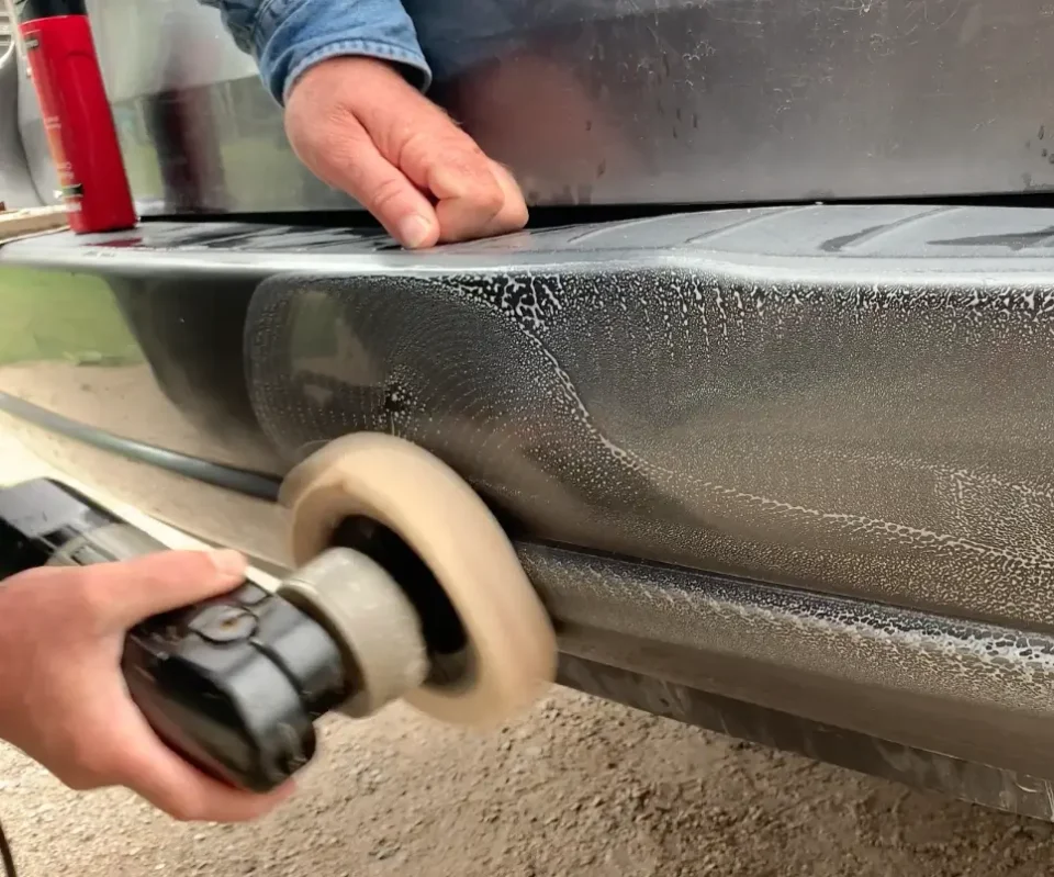 Person polishing scratched vehicle bumper.