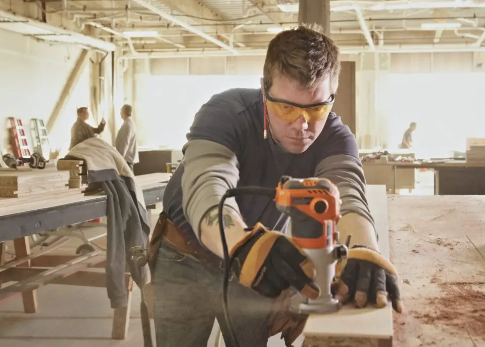 This carpenter is moving the router in the correct direction, moving from left to right on the piece of wood when the tool is hand-held.