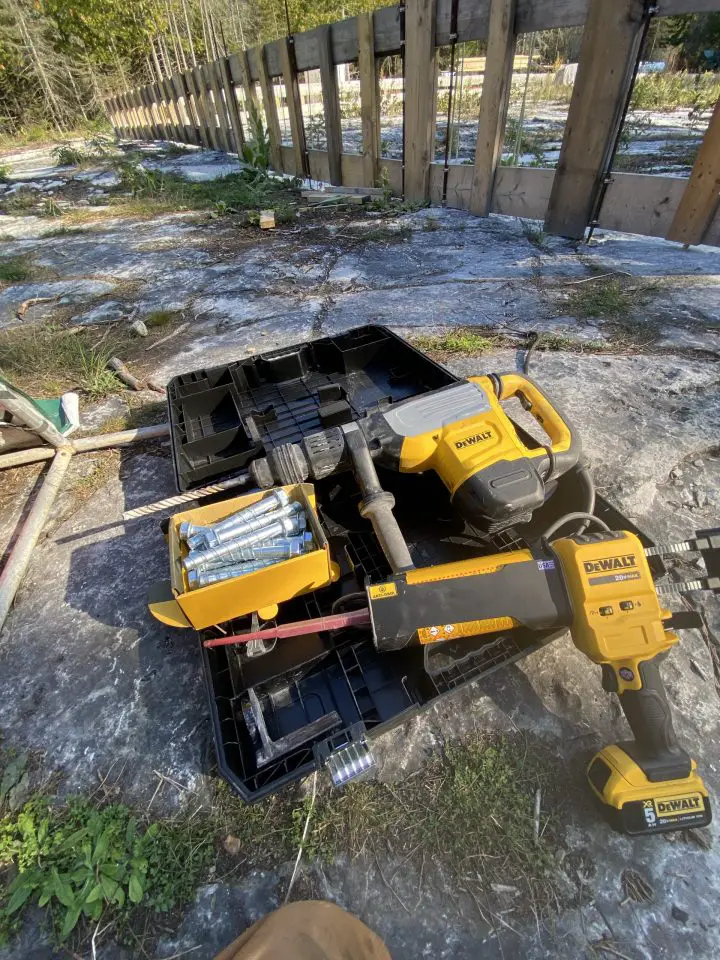 I used this combination of tools and supplies to anchor rebar to bedrock for a foundation I built. The tool at the top is a rotary hammer for boring holes in the rock, and the power caulking gun below is for injecting anchoring epoxy.