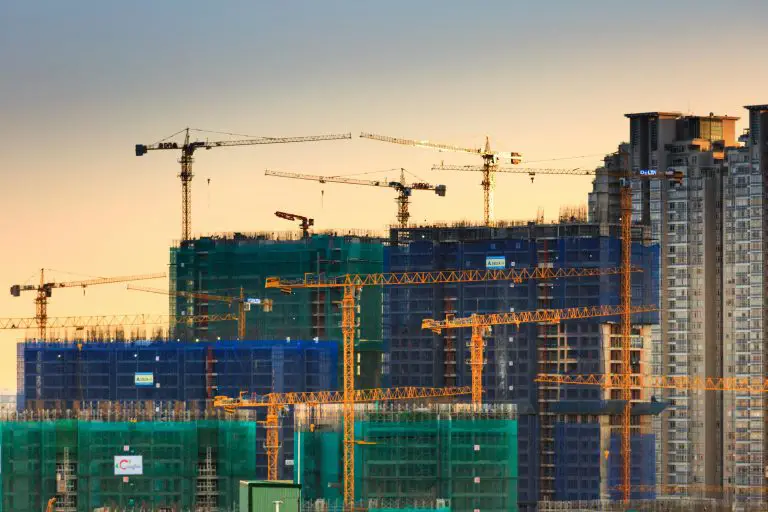 Cranes constructing high-rise buildings at sunset.