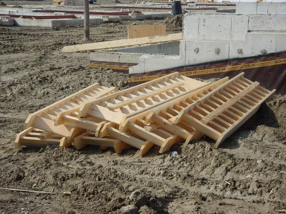 These pre-made wooden stair stringer and tread assemblies are sitting at a construction site waiting for installation in subdivision homes.