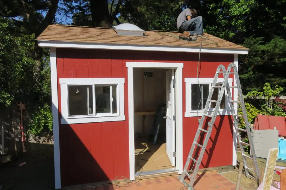 Red shed with ladder and man on roof.