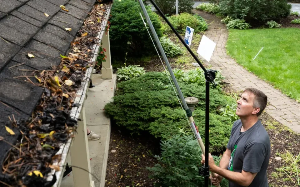 Person cleaning leaves from house gutter