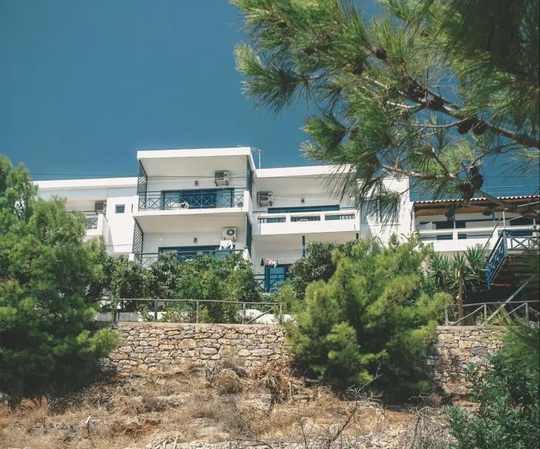 Modern white building with balconies and trees nearby.