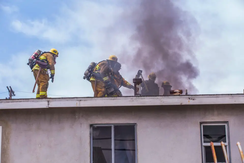 Firefighters working on smoking building roof.