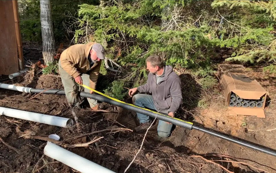 Two men measuring pipes in the forest