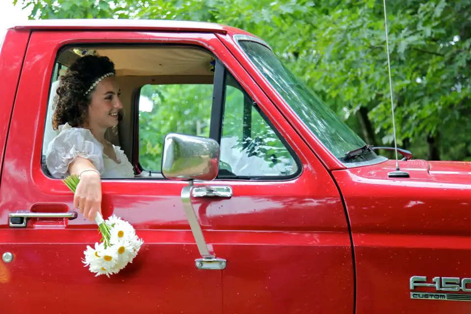 Smiling bride in red truck holding flowers.