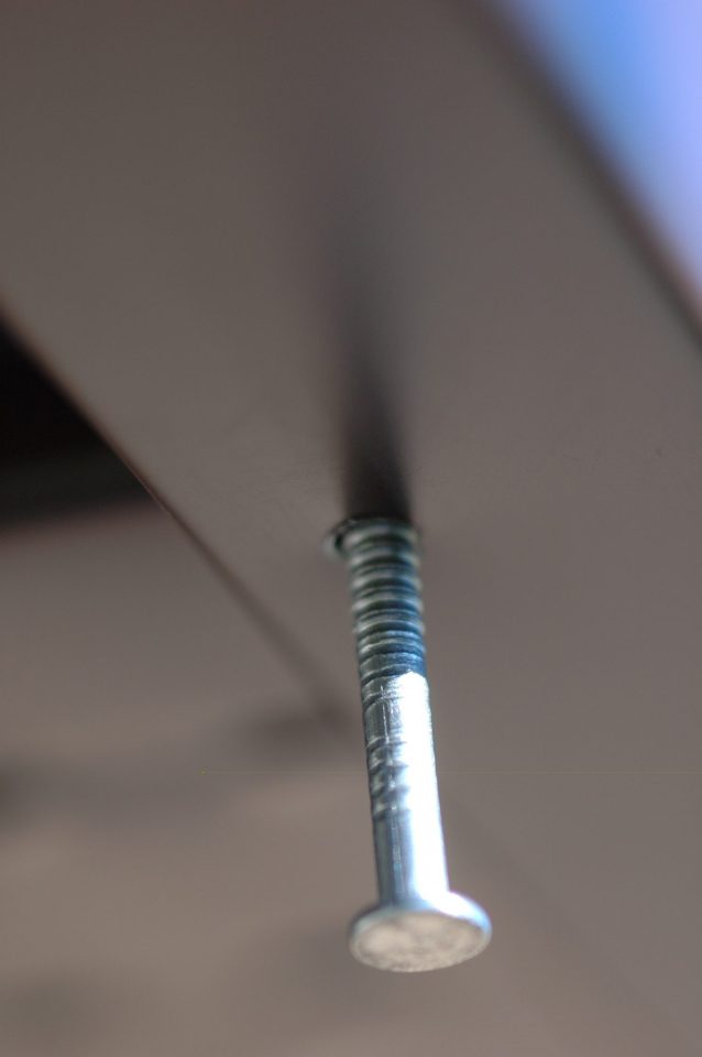 Stainless steel nail partially driven into over-sized hole in edge of fascia. The over-sized hole allows for expansion and contraction of aluminum.