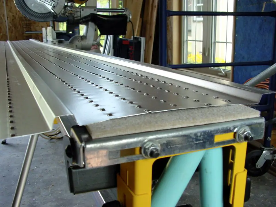 Aluminum soffit upside down and in place on the outfeed table of a chopsaw. Note the felt on the table protecting the painted surface.