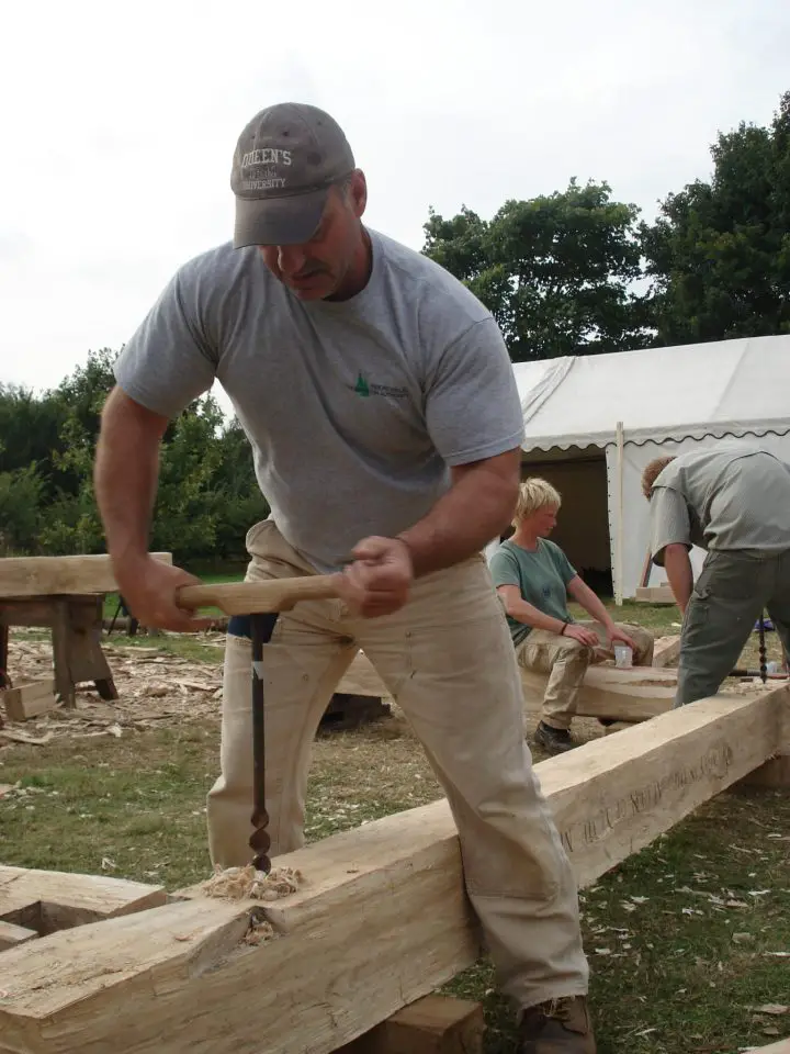 Timber framer Ray Gibbs boring a peg hole in a frame member. Today’s North American timber frame movement began with a revival of the craft in Massachusetts in the 1970s.