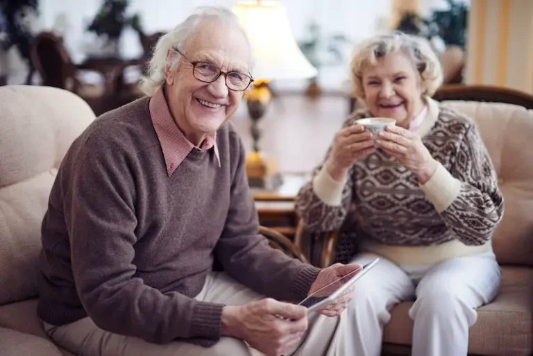 Smiling seniors relaxing with tablet and coffee.