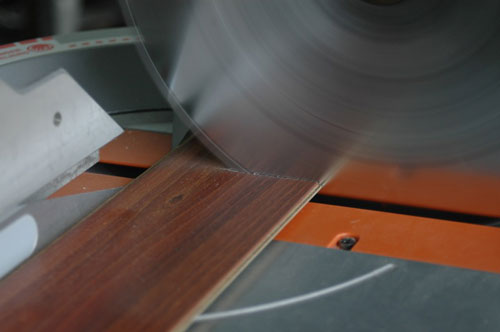 Laminate flooring being cut with a special blade in a chopsaw. Hand-held jigsaws are also great for cutting laminates. The smoothness of cuts doesn’t matter because all cut ends are covered by baseboard.
