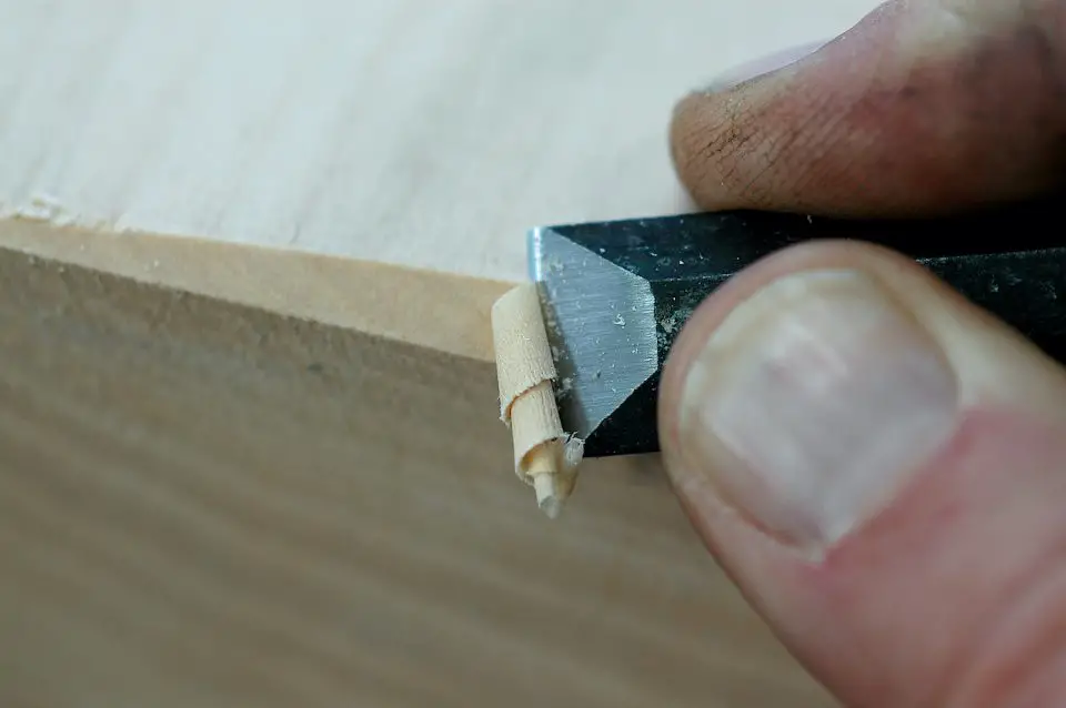 Close-up of hand carving wood with chisel.