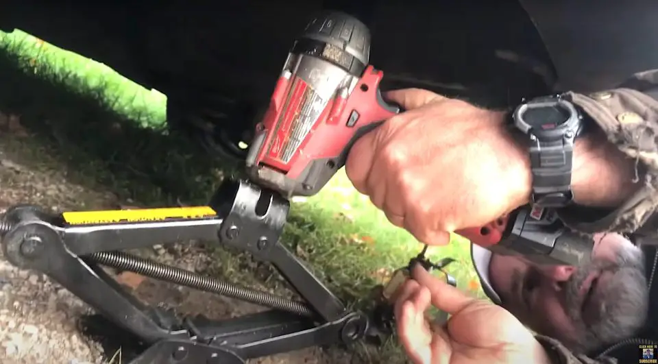 Man using impact driver with car jack.