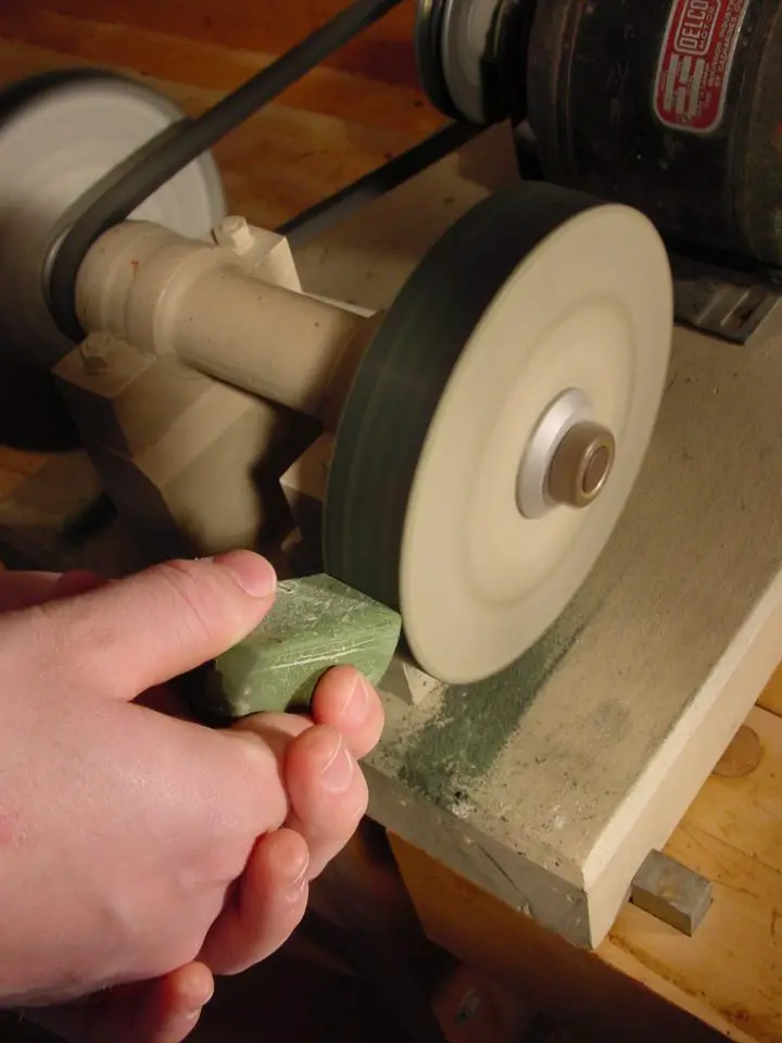 A buffing wheel uses very fine abrasive compound to polish the steel cutting edge and make it refined. Here I am applying some compound to the spinning edge of my hard felt buffing wheel.