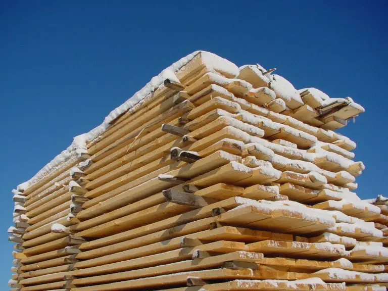 Stacked lumber covered with snow under blue sky.