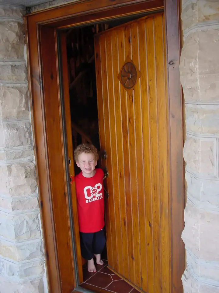 Child smiling at wooden door entrance.