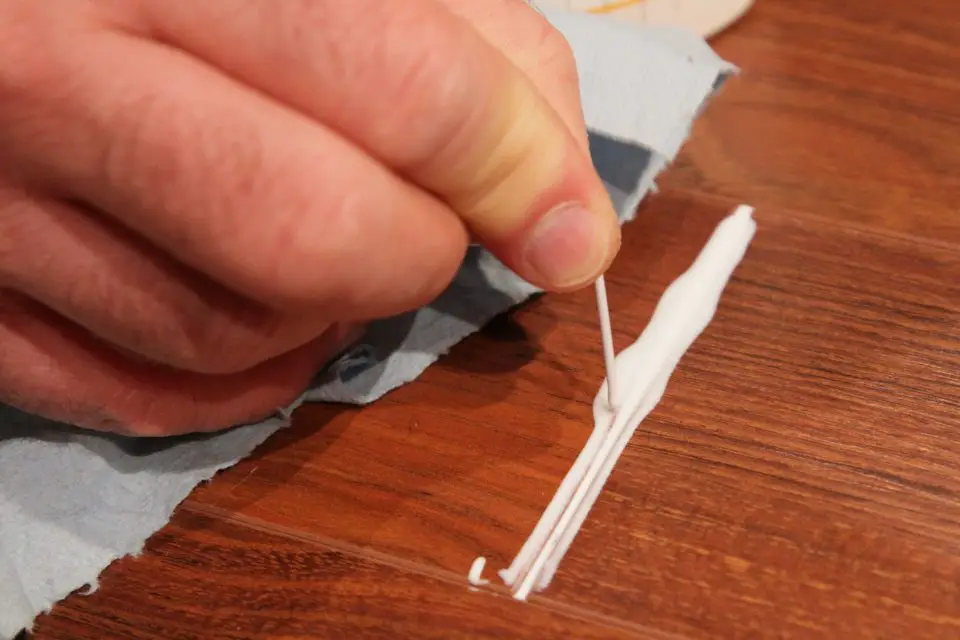 Applying wood filler to floor with toothpick.