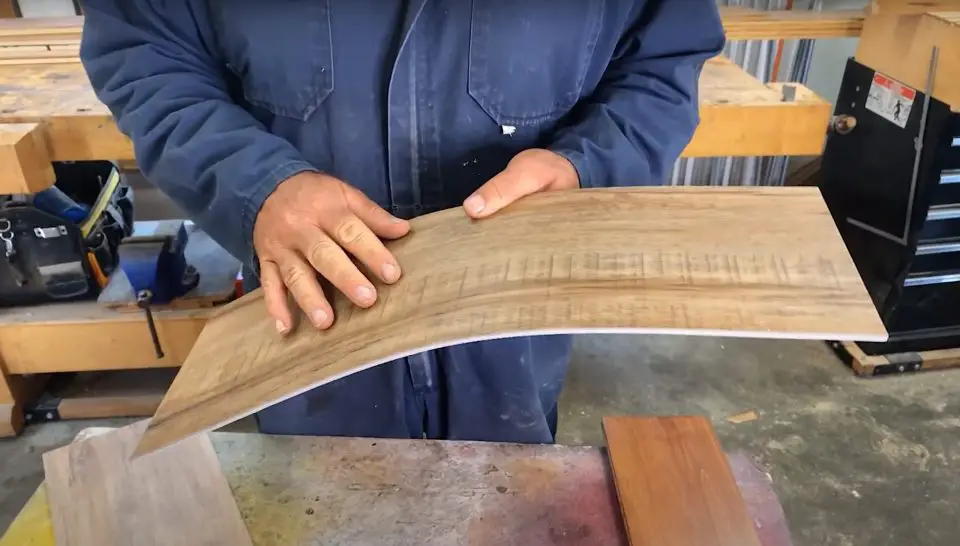 Person holding a curved wooden board in workshop.