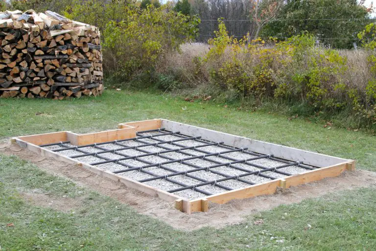 Woodpile beside prepared concrete foundation with rebar grid.