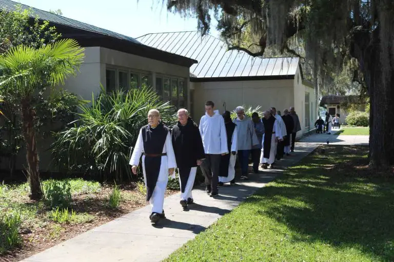Monks walking outside near a building and trees.