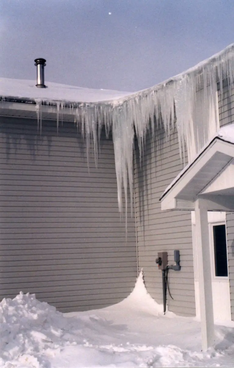 Ice and icicles hanging from house roof in winter.