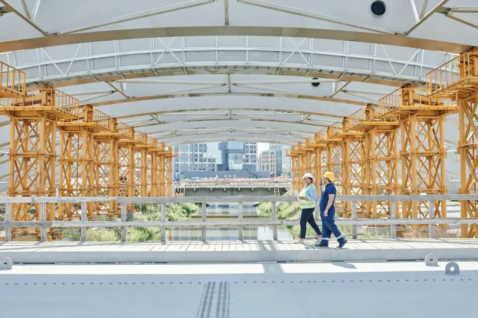 Two workers on large construction site bridge.