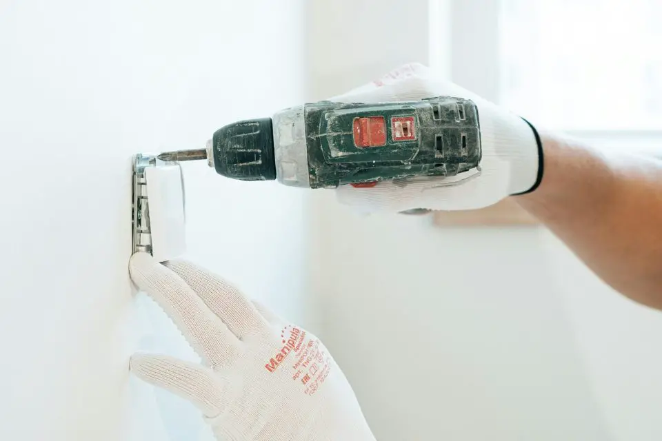 Person installing light switch with drill