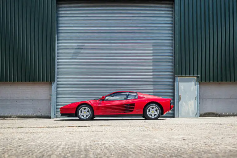 Red sports car parked outside industrial garage door.
