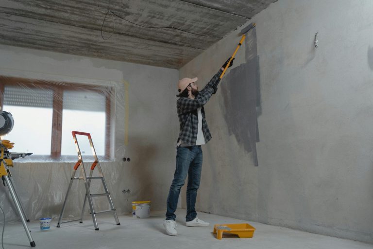 Person painting wall with grey paint roller indoors.