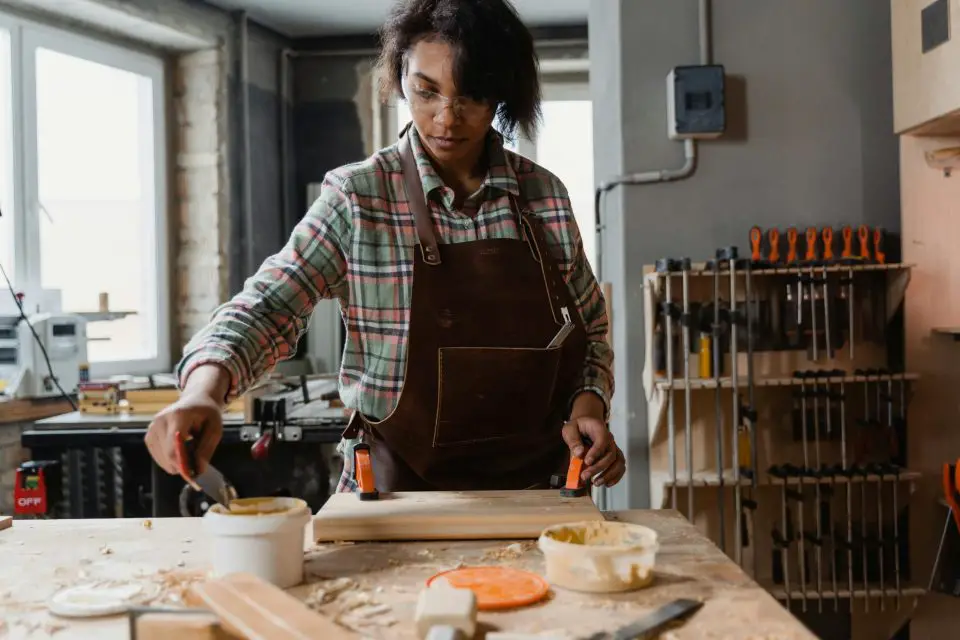 Woman woodworking in a workshop, wearing safety glasses.
