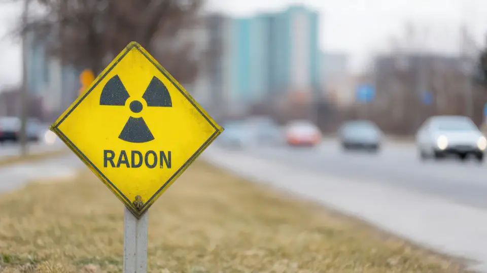 Radon warning sign on roadside with cars passing.