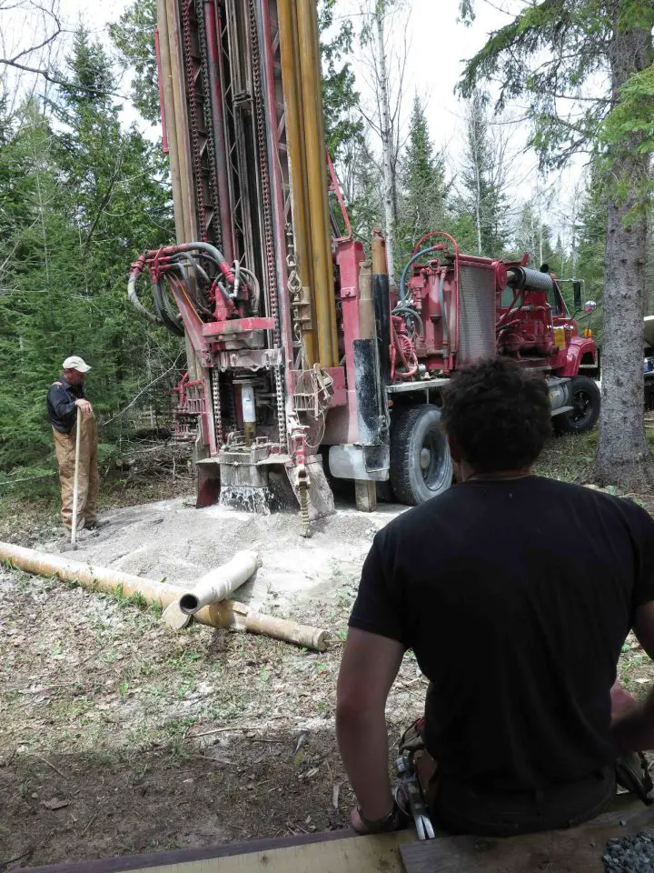 Workers operating a large drilling machine in forest.