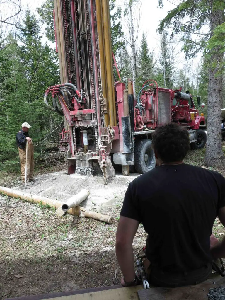 Workers operating a large drilling machine in forest.