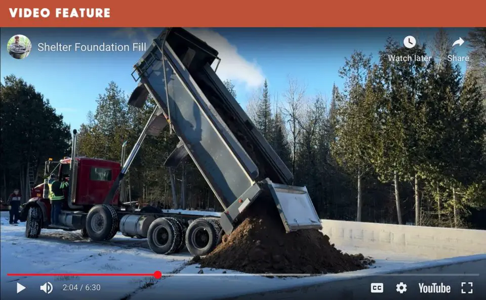 Dump truck unloading soil on snowy site.