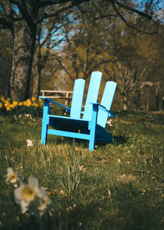 A bright blue Adirondack chair in a lush, sunlit park, perfect for relaxation.