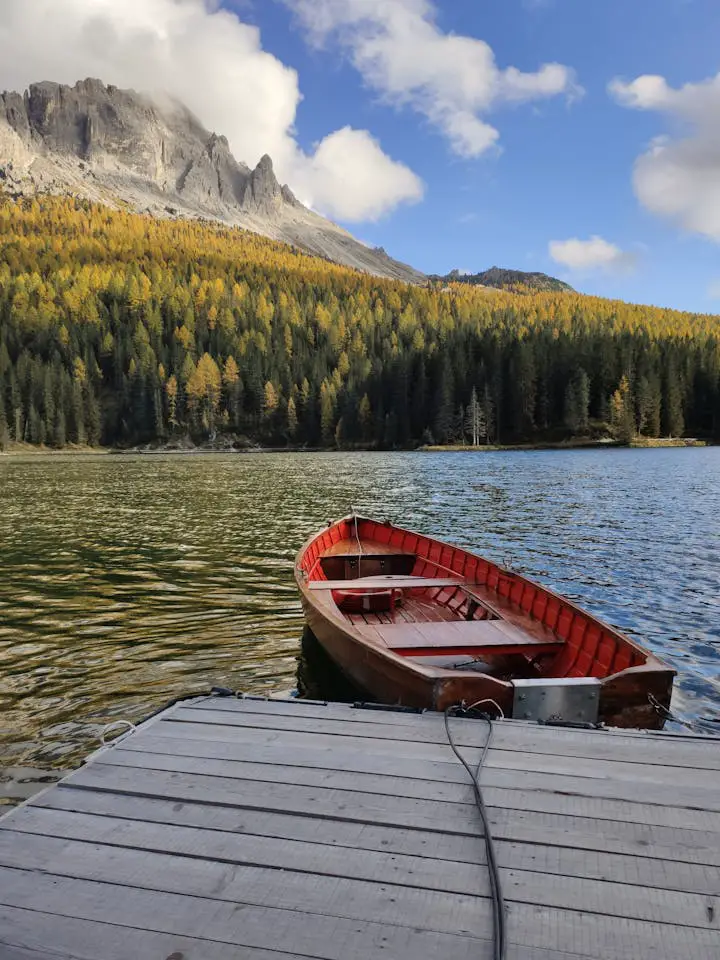 Tranquil scene of a wooden boat on a mountain lake dock with scenic forest and mountain backdrop.