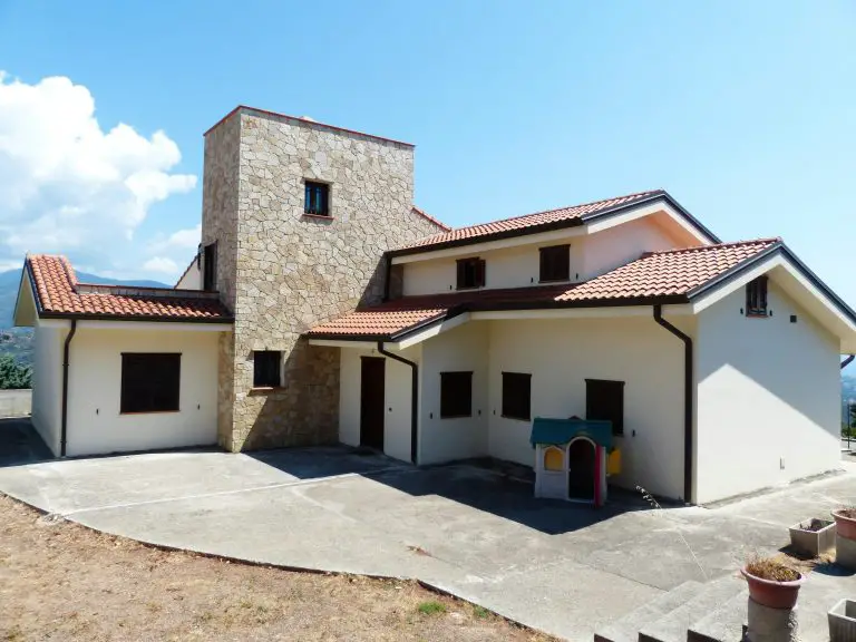 Modern house with stone chimney and red roof.